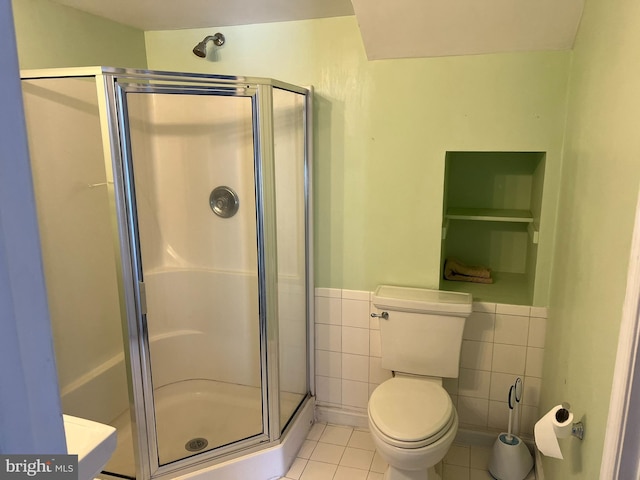 bathroom featuring tile patterned floors, toilet, a shower with door, and tile walls