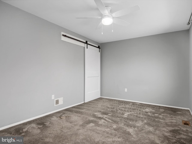 unfurnished bedroom with a barn door, ceiling fan, and carpet