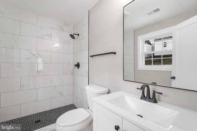 bathroom featuring tiled shower, toilet, and vanity