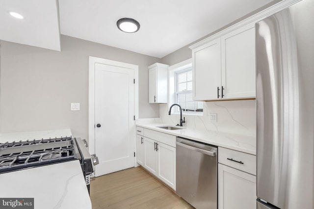 kitchen with appliances with stainless steel finishes, sink, white cabinets, light hardwood / wood-style flooring, and light stone counters