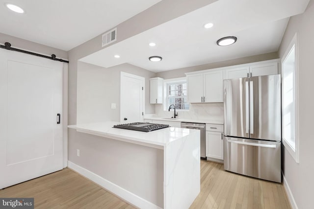 kitchen with sink, white cabinets, a barn door, light hardwood / wood-style floors, and stainless steel appliances