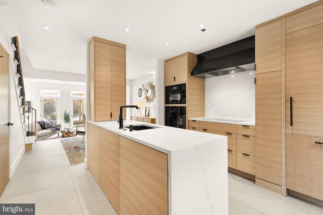 kitchen with sink, black appliances, light tile patterned floors, an island with sink, and wall chimney range hood