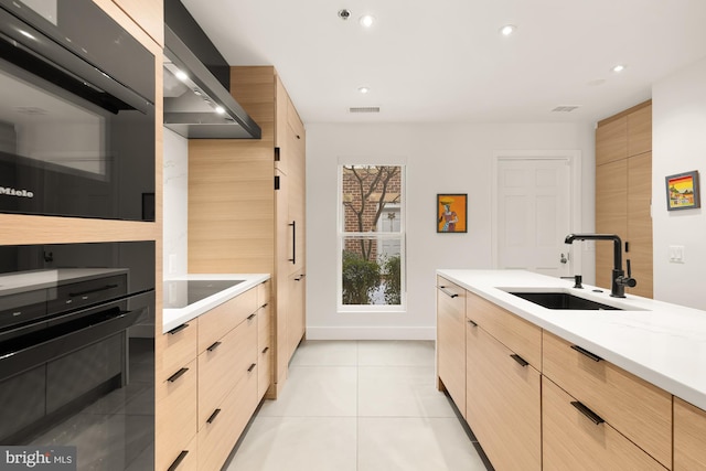 kitchen with light brown cabinetry, sink, light tile patterned floors, black appliances, and wall chimney exhaust hood