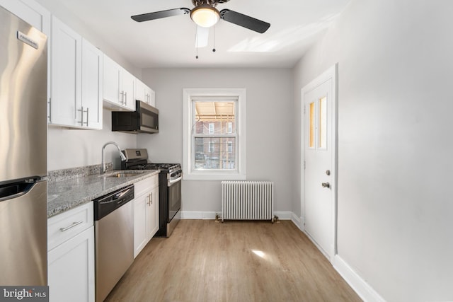 kitchen with appliances with stainless steel finishes, radiator, white cabinets, light stone counters, and light wood-type flooring