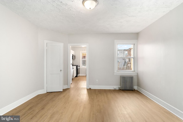 empty room with radiator heating unit, light hardwood / wood-style floors, and a textured ceiling