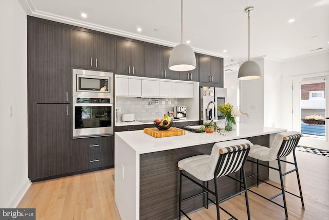 kitchen featuring a kitchen island with sink, pendant lighting, dark brown cabinetry, and stainless steel appliances