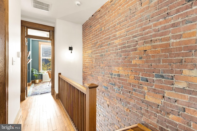 hallway with light wood-type flooring and brick wall