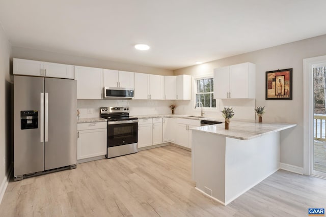 kitchen with kitchen peninsula, light stone counters, white cabinets, and appliances with stainless steel finishes