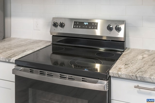 room details featuring stainless steel electric stove, white cabinets, decorative backsplash, and light stone countertops