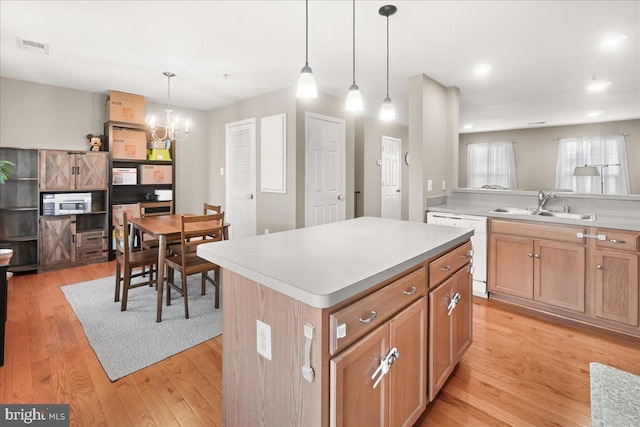 kitchen featuring a kitchen island, decorative light fixtures, dishwasher, sink, and light hardwood / wood-style floors