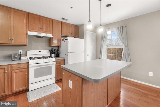 kitchen with pendant lighting, white appliances, a center island, and light hardwood / wood-style flooring