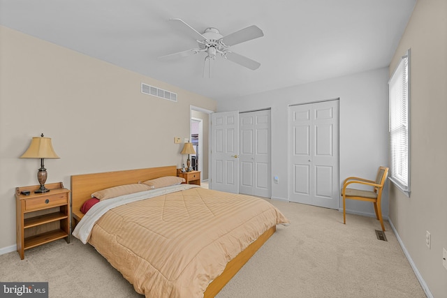 bedroom with ceiling fan, light carpet, and two closets