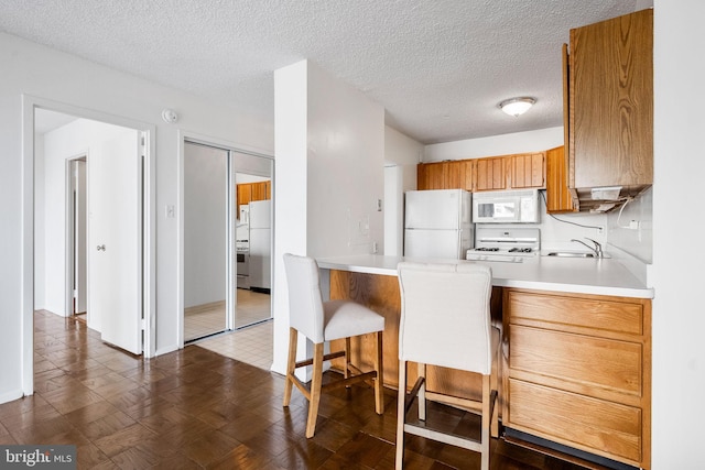 kitchen featuring a kitchen bar, sink, a textured ceiling, kitchen peninsula, and white appliances