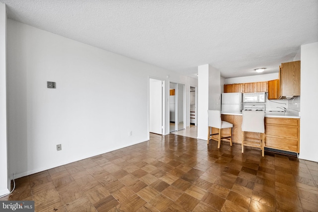 kitchen with dark parquet flooring, sink, a textured ceiling, and white appliances