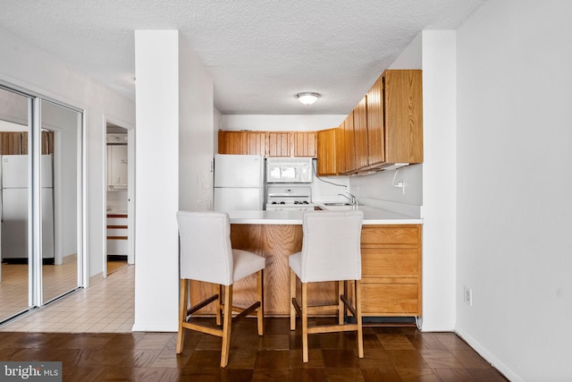 kitchen featuring sink, a breakfast bar area, white appliances, kitchen peninsula, and a textured ceiling