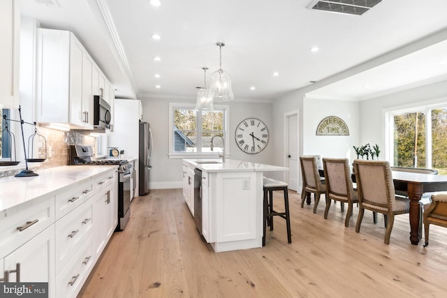 kitchen with a kitchen island with sink, decorative light fixtures, stainless steel appliances, and white cabinets