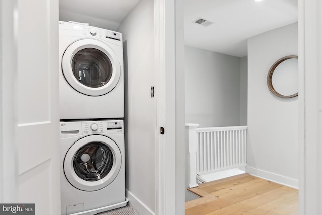 clothes washing area featuring wood-type flooring and stacked washer / dryer