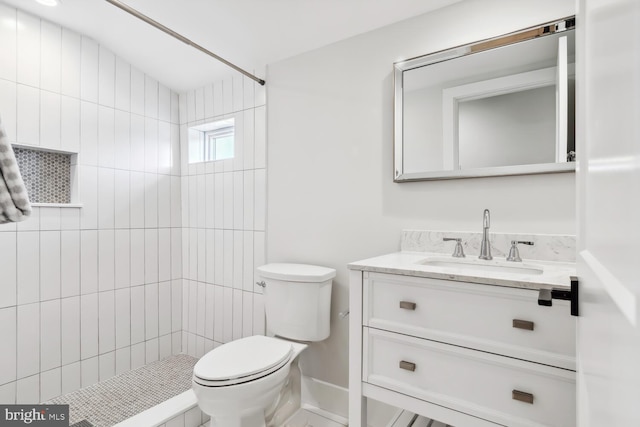 bathroom featuring vanity, a tile shower, and toilet