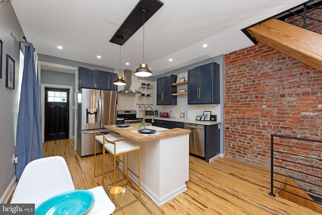 kitchen featuring a breakfast bar, appliances with stainless steel finishes, a kitchen island with sink, wood counters, and wall chimney exhaust hood