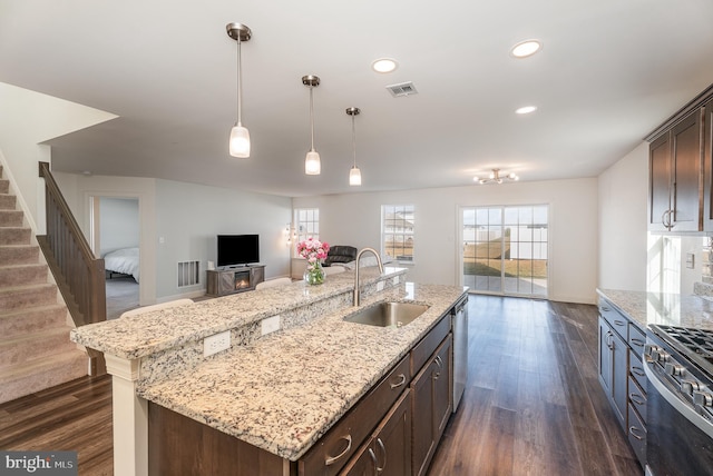 kitchen with dark brown cabinetry, sink, light stone counters, appliances with stainless steel finishes, and an island with sink