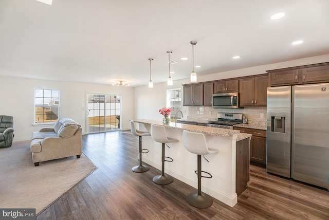 kitchen with decorative light fixtures, an island with sink, a breakfast bar area, light stone counters, and stainless steel appliances