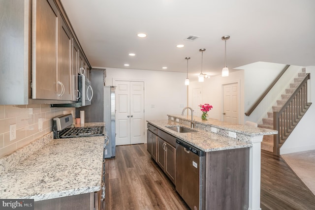 kitchen with appliances with stainless steel finishes, decorative light fixtures, sink, a kitchen island with sink, and light stone counters