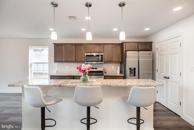 kitchen featuring appliances with stainless steel finishes, dark hardwood / wood-style floors, a center island, light stone counters, and decorative light fixtures