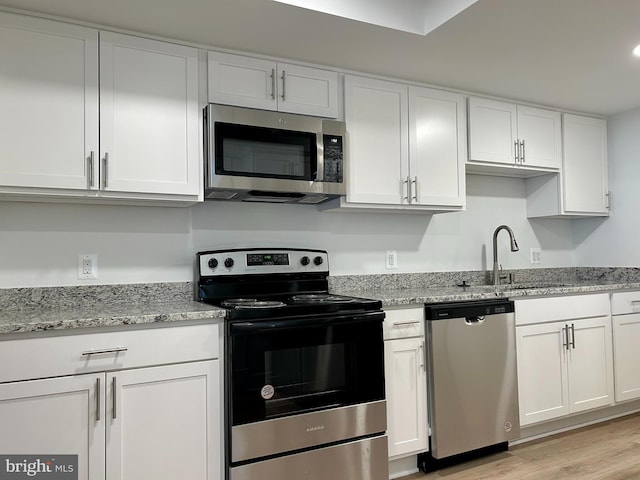 kitchen with light stone countertops, white cabinets, light wood-type flooring, sink, and stainless steel appliances