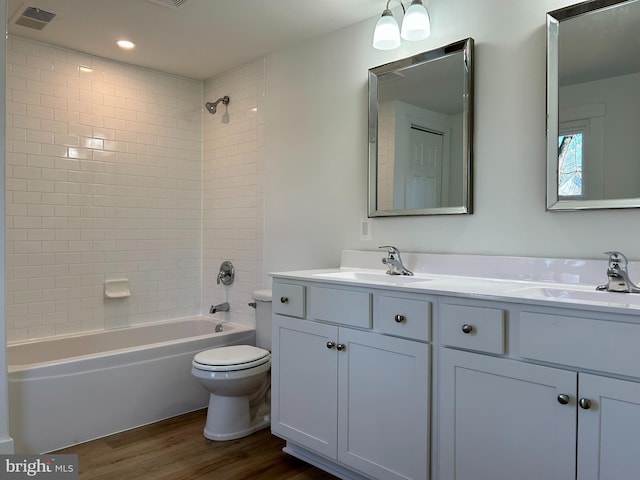 full bathroom featuring hardwood / wood-style floors, tiled shower / bath combo, vanity, and toilet