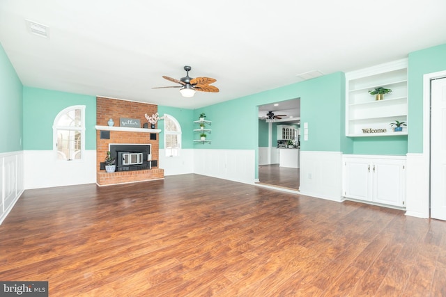 unfurnished living room with hardwood / wood-style flooring, a brick fireplace, built in features, and ceiling fan