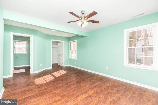 unfurnished bedroom featuring ceiling fan, dark hardwood / wood-style flooring, and a walk in closet