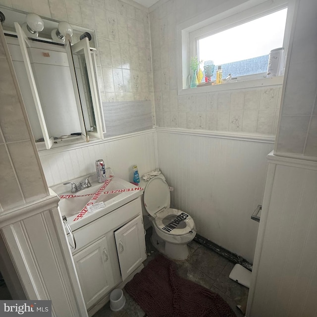 half bath featuring toilet, tile patterned floors, vanity, and wainscoting