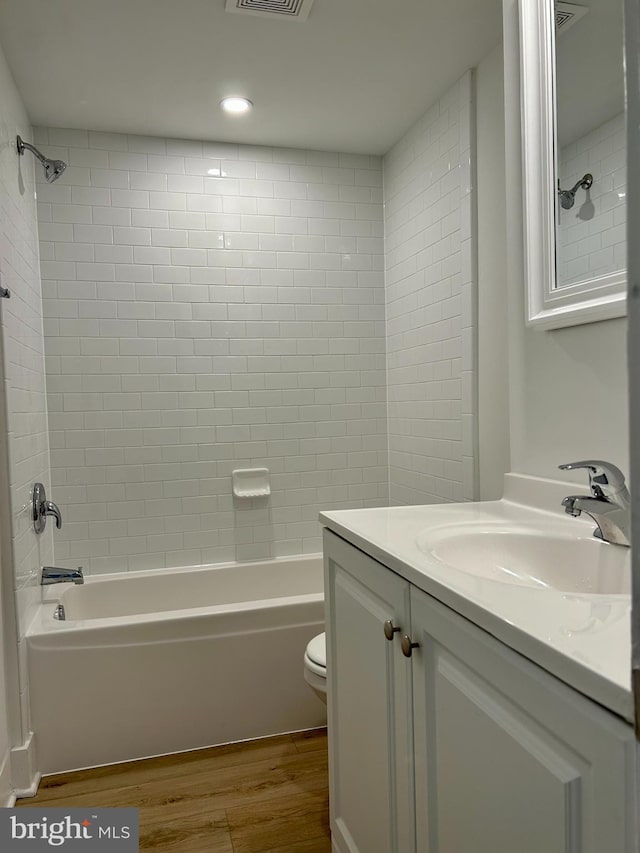 full bathroom featuring wood-type flooring, toilet, tiled shower / bath, and vanity