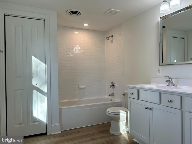 full bathroom with wood-type flooring, tiled shower / bath combo, vanity, and toilet