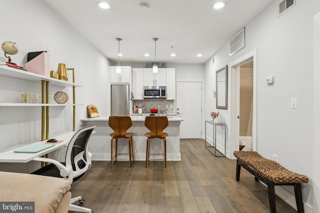 kitchen with hanging light fixtures, white cabinets, tasteful backsplash, a breakfast bar, and stainless steel appliances