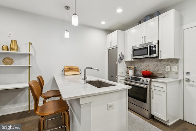 kitchen with pendant lighting, appliances with stainless steel finishes, sink, white cabinets, and light stone countertops