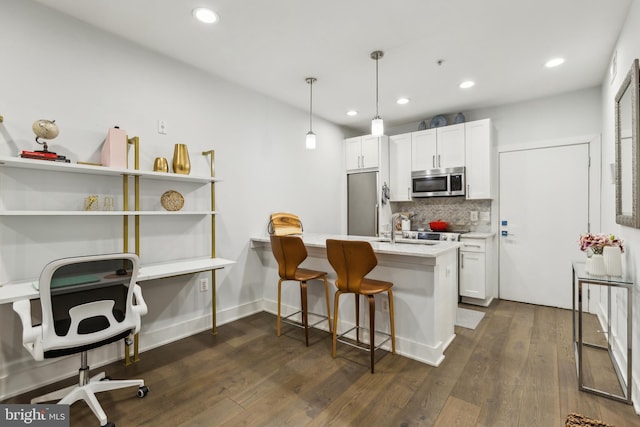 kitchen featuring pendant lighting, appliances with stainless steel finishes, white cabinets, a kitchen bar, and decorative backsplash