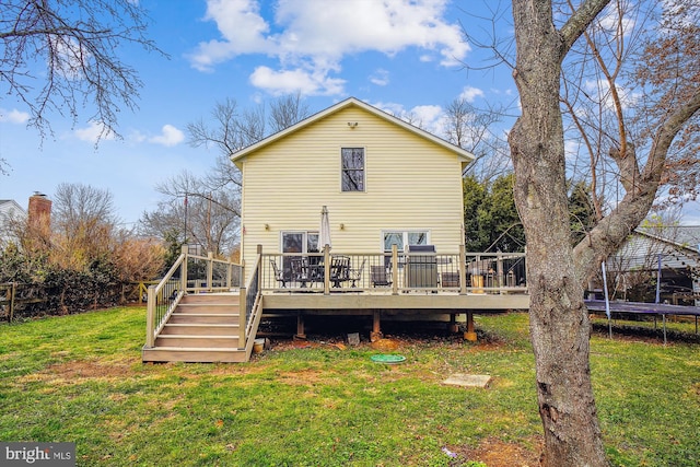 rear view of house featuring a trampoline, a wooden deck, and a yard