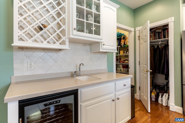 kitchen with white cabinetry, sink, beverage cooler, decorative backsplash, and light hardwood / wood-style flooring