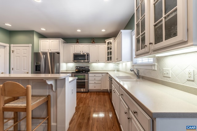 kitchen with a breakfast bar, sink, white cabinets, stainless steel appliances, and dark wood-type flooring