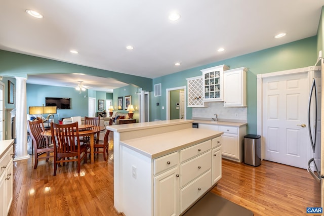 kitchen with ornate columns, white cabinets, a center island, ceiling fan, and light wood-type flooring