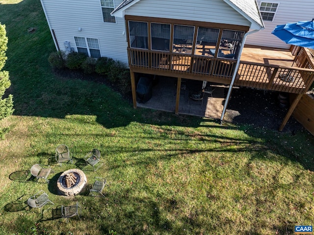 rear view of house featuring a wooden deck, a sunroom, a yard, and a fire pit