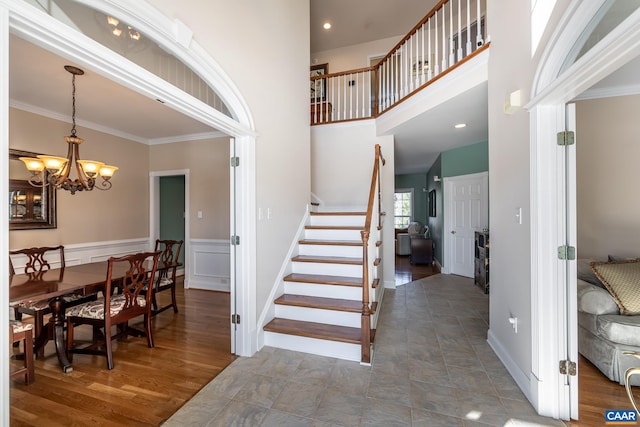 stairway featuring a high ceiling, ornamental molding, hardwood / wood-style floors, and a chandelier