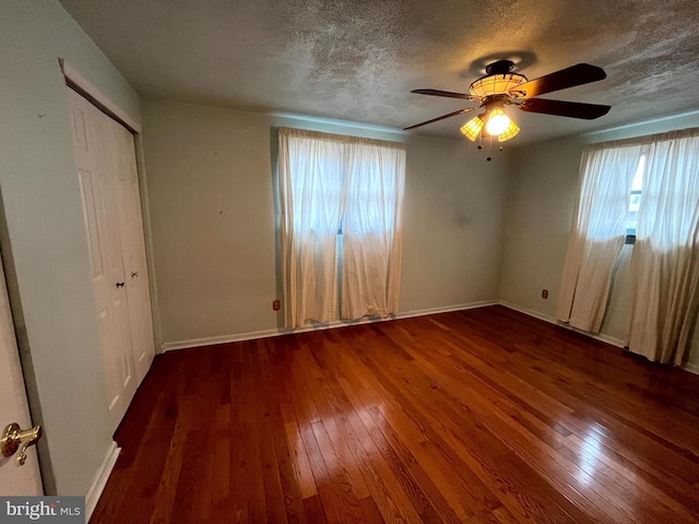 unfurnished bedroom with multiple windows, a textured ceiling, dark wood-type flooring, and ceiling fan