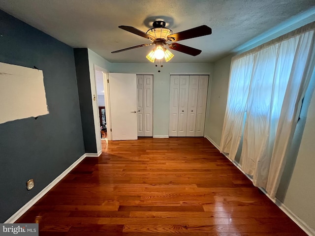 unfurnished bedroom with multiple closets, hardwood / wood-style flooring, a textured ceiling, and ceiling fan