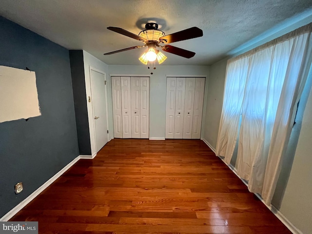 unfurnished bedroom with ceiling fan, two closets, a textured ceiling, and hardwood / wood-style flooring