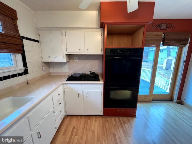 kitchen featuring white cabinets, black appliances, light hardwood / wood-style floors, sink, and backsplash