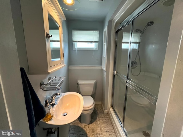 bathroom featuring a shower with shower door, sink, and toilet