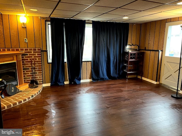 unfurnished living room with a drop ceiling, a healthy amount of sunlight, wooden walls, and dark hardwood / wood-style floors