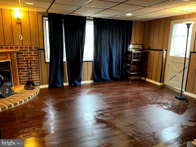 unfurnished living room featuring a fireplace, wood walls, a drop ceiling, and dark hardwood / wood-style flooring